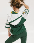 A woman wearing a green and white hoodie with a half-zip design, kangaroo pocket, and decorative woven ribbons.