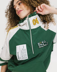 A woman wearing a green and white hoodie with a half-zip design, kangaroo pocket, and decorative woven ribbons.