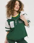 A woman wearing a green and white hoodie with a half-zip design, kangaroo pocket, and decorative woven ribbons.
