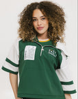 A woman wearing a green and white hoodie with a half-zip design, kangaroo pocket, and decorative woven ribbons.