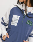 A woman wearing a blue and white hoodie with a half-zip feature and a kangaroo pocket, paired with a white skirt.