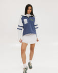 A woman wearing a blue and white hoodie with a half-zip feature and a kangaroo pocket, paired with a white skirt.