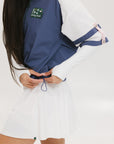 A person wearing a two-tone hoodie with a predominantly white body and blue sleeves. The hoodie features a drawstring hood and a small brand logo on the upper left side.
