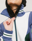 A woman wearing a half zip sports top with colorblocking in blue, white, and green, and ribbed detailing around the collar, cuffs, and hem.