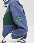 A woman wearing a half zip sports top with colorblocking in blue, white, and green, and ribbed detailing around the collar, cuffs, and hem.