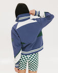 A woman wearing a half zip sports top with colorblocking in blue, white, and green, and ribbed detailing around the collar, cuffs, and hem.
