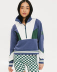 A woman wearing a half zip sports top with colorblocking in blue, white, and green, and ribbed detailing around the collar, cuffs, and hem.