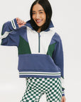 A woman wearing a half zip sports top with colorblocking in blue, white, and green, and ribbed detailing around the collar, cuffs, and hem.