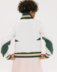 A woman wearing a white half zip sports top with green color blocking and ribbed detailing around the collar, cuffs, and hem. The top features half sleeve design with a signature logo on the chest.