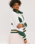 A woman wearing a white half zip sports top with green color blocking and ribbed detailing around the collar, cuffs, and hem. The top features half sleeve design with a signature logo on the chest.