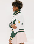 A woman wearing a white half zip sports top with green color blocking and ribbed detailing around the collar, cuffs, and hem. The top features half sleeve design with a signature logo on the chest.