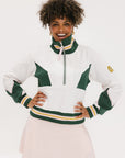 A woman wearing a white half zip sports top with green color blocking and ribbed detailing around the collar, cuffs, and hem. The top features half sleeve design with a signature logo on the chest.