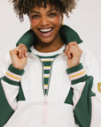 A woman wearing a white half zip sports top with green color blocking and ribbed detailing around the collar, cuffs, and hem. The top features half sleeve design with a signature logo on the chest.