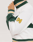 A woman wearing a white half zip sports top with green color blocking and ribbed detailing around the collar, cuffs, and hem. The top features half sleeve design with a signature logo on the chest.