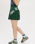 A person wearing a green skirt with a mesh back, paired with a blue top and green sneakers. The skirt has a high waist and a mid-thigh length cut.