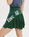 A person wearing a green skirt with a mesh back, paired with a blue top and green sneakers. The skirt has a high waist and a mid-thigh length cut.