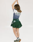 A person wearing a green skirt with a mesh back, paired with a blue top and green sneakers. The skirt has a high waist and a mid-thigh length cut.