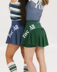 Two models wearing a blue and green skirt with a mesh back. The image focuses on the skirt which has a sports-inspired design.