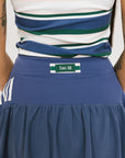 A person wearing a blue skirt with a mesh back, along with a striped top and white socks with green stripes. The image focuses on the skirt which has a sports-inspired design.