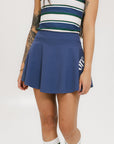 A person wearing a blue skirt with a mesh back, along with a striped top and white socks with green stripes. The image focuses on the skirt which has a sports-inspired design.