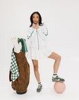 A person wearing a white angel skirt with a white top, posing with a brown bag and a pink ball at their feet.