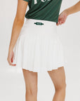 A person wearing a white skirt with a mesh back, paired with a green top and matching green and white sneakers. The skirt has a grippy elastic hem and built-in biddy shorties with pockets.