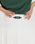 A person wearing a white skirt with a mesh back, paired with a green top and matching green and white sneakers. The skirt has a grippy elastic hem and built-in biddy shorties with pockets.