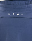 A woman is wearing a navy blue skirt with a built-in pair of biddy shorties featuring a white and green logo. She has a round drawstring cord at the waist and stitched logos on the back.