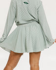 Model wearing the patty skirt in green seersucker. Featuring a green drawstring, buttons down the front, and a fore all logo on the bottom of the skirt.
