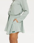 Model wearing the patty skirt in green seersucker. Featuring a green drawstring, buttons down the front, and a fore all logo on the bottom of the skirt.