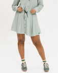 A person wearing a green striped skirt with a flat drawstring, faux buttons down the front, and side seam pockets. The skirt has a knee-length cut and the person is also wearing a green and white striped top with the skirt.