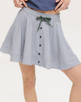 A seersucker skirt with subtle stripes, featuring a flat drawstring, faux buttons down the front, and side seam pockets.