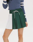 A woman wearing a pleated green and white skirt with a round drawstring waist, colorblocking, and a 'Chasing Balls' icon patch on the back.