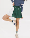 A woman wearing a pleated green and white skirt with a round drawstring waist, colorblocking, and a 'Chasing Balls' icon patch on the back.