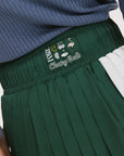 A woman wearing a pleated green and white skirt with a round drawstring waist, colorblocking, and a 'Chasing Balls' icon patch on the back.