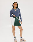 A person wearing a rose pleated green skirt with a blue and white striped sweater, standing against a white background.