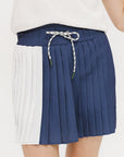 A pleated skirt with colorblocking in indigo and white, featuring a round drawstring cord at the waist and a 'Chasing Balls' icon patch on the back.
