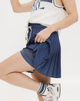 A person wearing a blue rose pleated skirt with a white top and sneakers. The skirt reaches mid-thigh and has a pleated design.