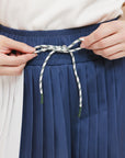 A pleated skirt with colorblocking in indigo and white, featuring a round drawstring cord at the waist and a 'Chasing Balls' icon patch on the back.
