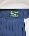 A pleated skirt with colorblocking in indigo and white, featuring a round drawstring cord at the waist and a 'Chasing Balls' icon patch on the back.