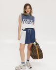 A pleated skirt with colorblocking in indigo and white, featuring a round drawstring cord at the waist and a 'Chasing Balls' icon patch on the back.