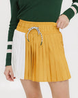 A person wearing a mustard pleated skirt with colorblocking, featuring a round drawstring cord and pockets.