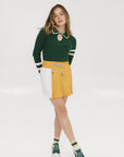 A person wearing a mustard pleated skirt with colorblocking, featuring a round drawstring cord.