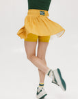 A person wearing a mustard pleated skirt with colorblocking, featuring a round drawstring cord.