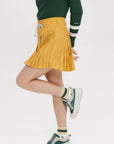 A person wearing a mustard pleated skirt with colorblocking, featuring a round drawstring cord.