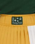 A person wearing a mustard pleated skirt with colorblocking, featuring a round drawstring cord.