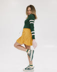 A person wearing a mustard pleated skirt with colorblocking, featuring a round drawstring cord.