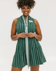 A woman smiling and wearing a sleeveless, pinstripe green dress with a pleated skirt, white trim, and applique logos.