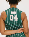 A woman wearing a sleeveless, pinstripe green dress with a pleated skirt, white trim, and applique logos.