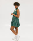 A woman wearing a sleeveless, pinstripe green dress with a pleated skirt, white trim, and applique logos.
